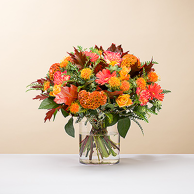 Les teintes flamboyantes de l'automne abondent dans ce bouquet vibrant, fait à la main, dans les tons orange, bordeaux, rose vif et jaune.